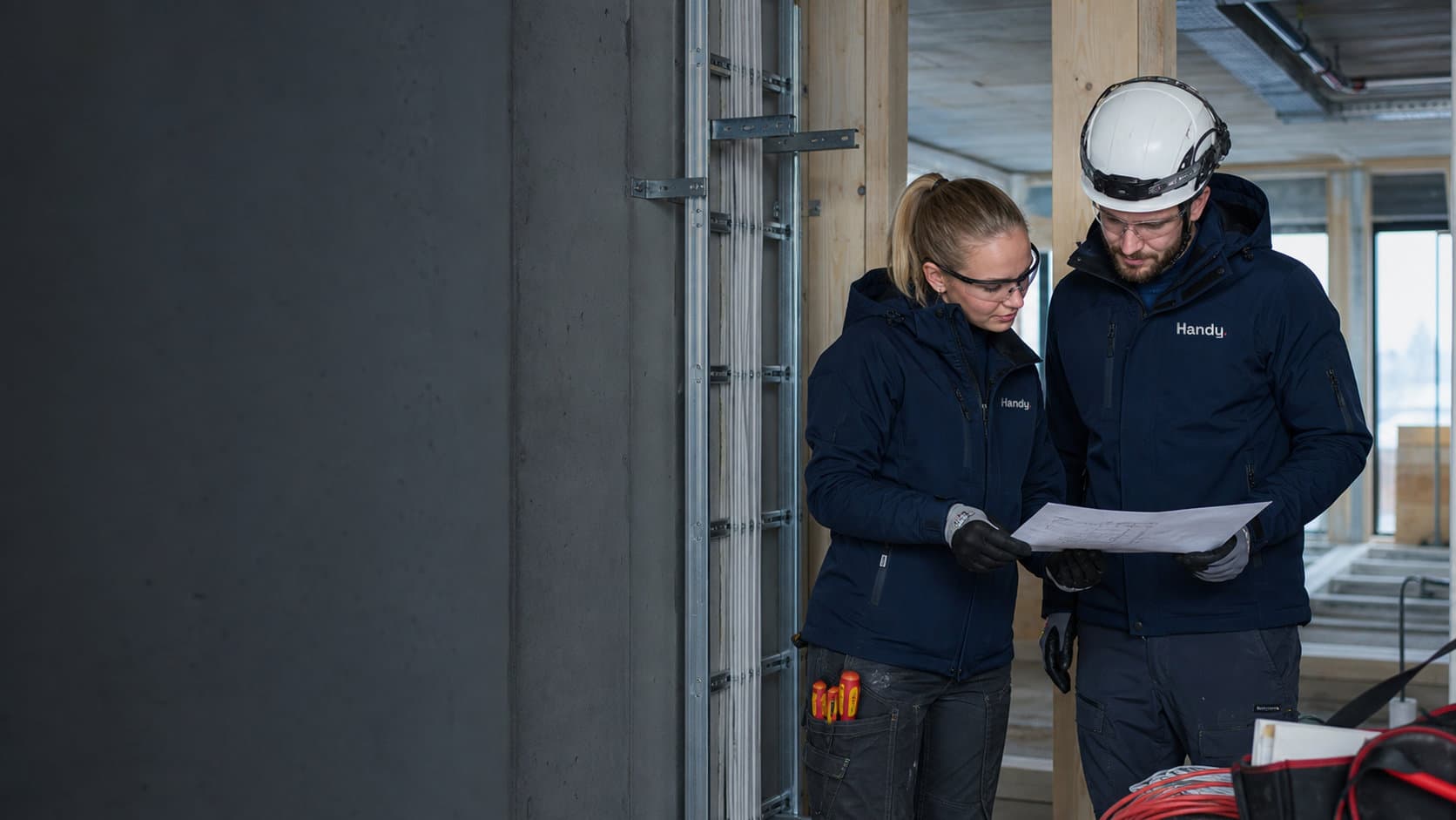 To Handy-elektrikere gjennomgår en installasjonsplan på byggeplass